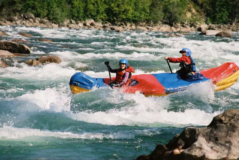 Two paddlers in helmets run whitewater in a red, blue and yellow inflatable boat